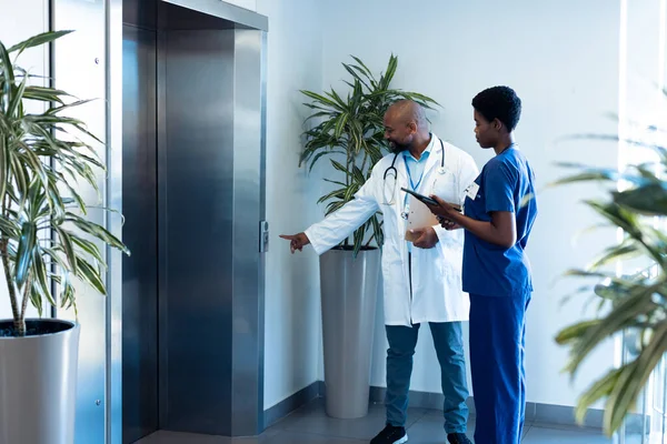 在医院走廊里笑着非洲裔美国男女医生叫电梯 医疗和保健服务 — 图库照片
