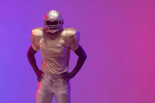 African american male american football player wearing helmet with neon blue and purple lighting. Sport, movement, training and active lifestyle concept.