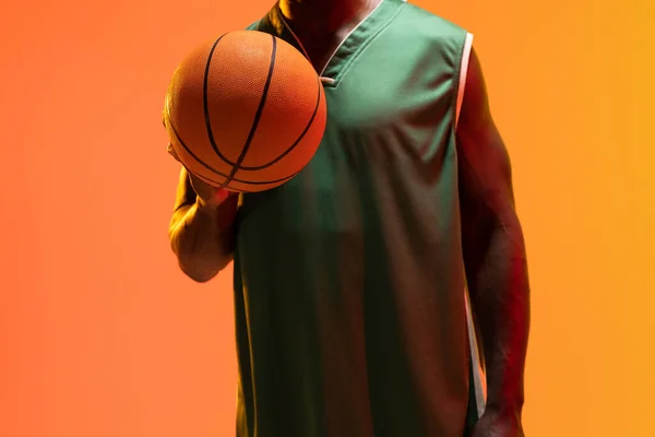 Obraz Środkowej Części Afrykańskiego Koszykarza Amerykańskiego Koszykówką Neonowym Pomarańczowym Tle — Zdjęcie stockowe