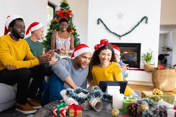 クリスマスにタブレットを使用してサンタの帽子と幸せな多様な友人 クリスマス お祝い 包容力とライフスタイルの概念 — ストック写真