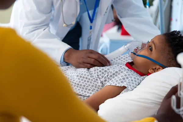 病院のベッドで人工呼吸器の息子の患者の横にアフリカ系アメリカ人の男性医師と母親 医療サービス — ストック写真