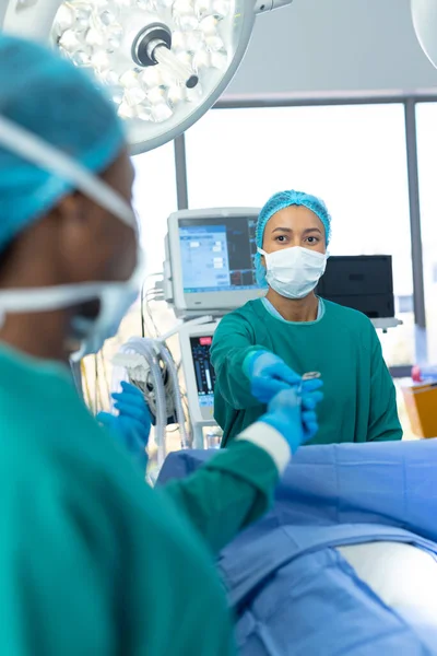 Vertical Biracial Feminino Cirurgião Passando Ferramenta Teatro Durante Operação Com — Fotografia de Stock