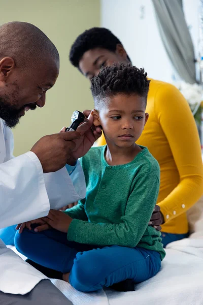 非裔美国男性医生用耳镜检查有母亲的男青年病人的耳朵 医疗和保健服务 — 图库照片