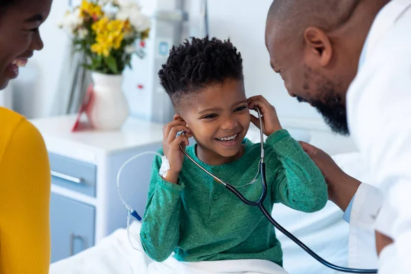 微笑着非洲裔美国母亲和儿子病人在医院试镜医生听诊器 医疗和保健服务 — 图库照片