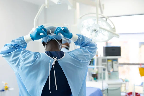 アフリカ系アメリカ人男性外科医のガウンと手袋を劇場でマスクに結びつけるの背面図 スペースをコピーします 医療サービス — ストック写真