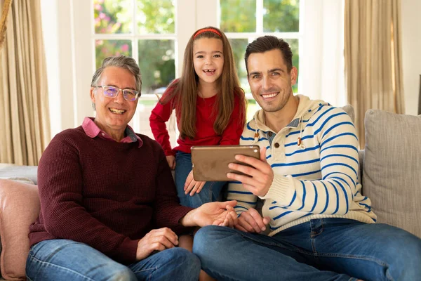 照片上是快乐的高加索人祖父 父亲和女儿坐在沙发上与平板电脑 家庭与共同度过美好时光的概念 — 图库照片
