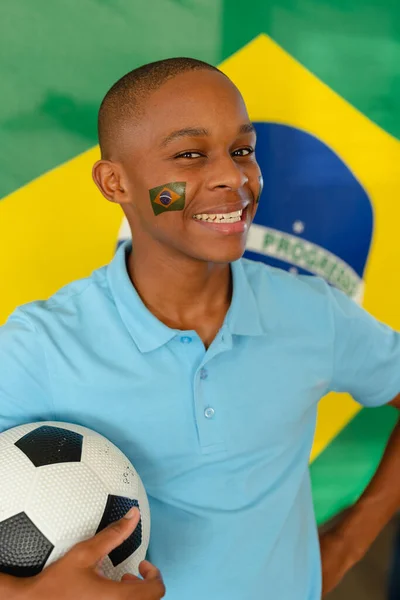 ブラジルとサッカーの旗を持つ幸せなアフリカ系アメリカ人男性ティーンエイジャーの肖像画 質の高い時間を家だけで過ごす — ストック写真