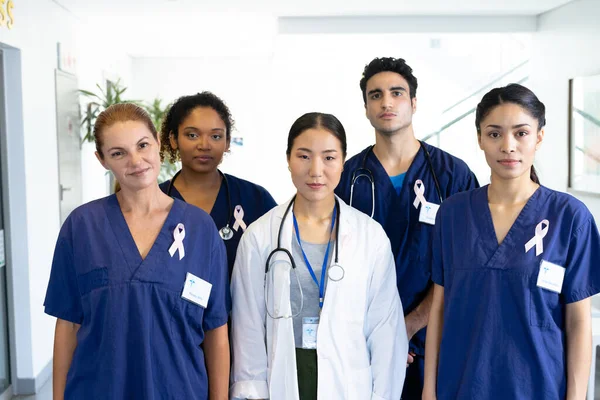 Portrait of diverse group of healthcare workers wearing cancer ribbons standing in hospital corridor. Hospital, medical and healthcare services.