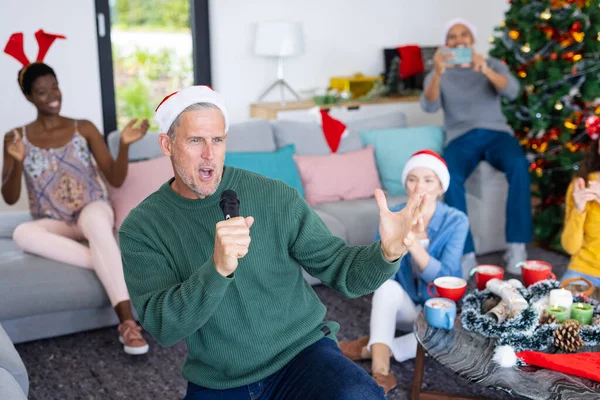 画面中快乐的高加索人和不同的朋友在家里唱卡拉Ok庆祝圣诞节 圣诞节 庆祝活动 包容和生活方式概念 — 图库照片
