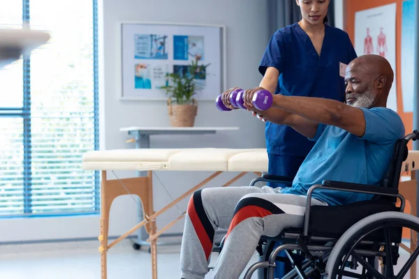 多様な女性理学療法士は ダンベル コピースペースを使用して車椅子の高齢男性患者を支援します 医療サービス — ストック写真