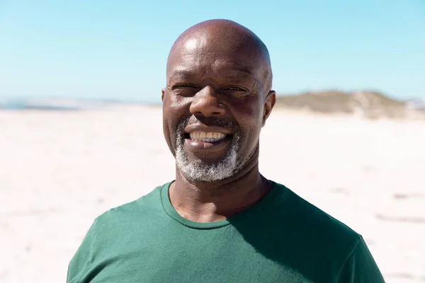 stock image Portrait of african american bald senior man smiling while spending weekend at beach under clear sky. Copy space, unaltered, lifestyle, vacation, retirement, summer, enjoyment and nature concept.
