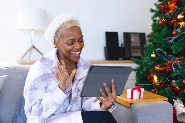 快乐的非洲裔美国女人戴着圣塔克洛斯帽 用平板电脑进行视频通话 一个人在圣诞节消磨时光 — 图库照片