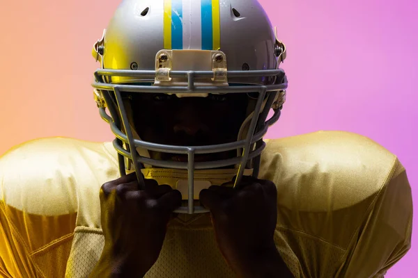 African american male american football player wearing helmet with neon yellow and purple lighting. Sport, movement, training and active lifestyle concept.