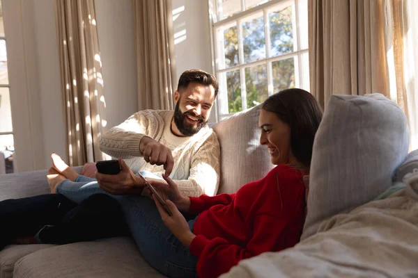 スマートフォンやタブレットを使用して リビングルームの笑いのソファに座って幸せな白人のカップル 国内生活 共生の概念 — ストック写真