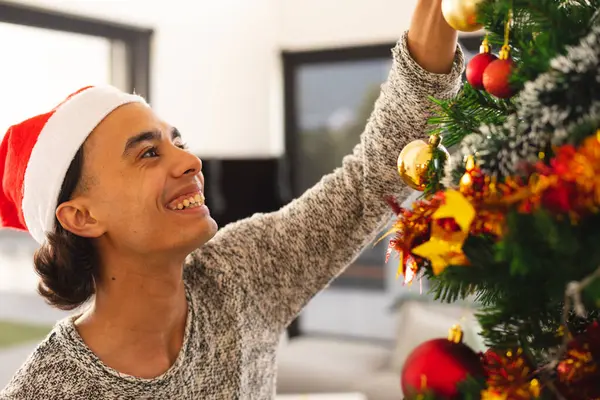 サンタの帽子をかぶった幸せな出産の男は リビングルームでクリスマスツリーを飾る クリスマスだけで質の高い時間を過ごす — ストック写真