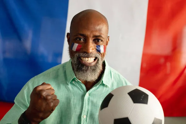一个快乐的资深非洲裔美国人的画像 他拿着法国国旗和足球坐在那里 独自在家度过美好时光 — 图库照片