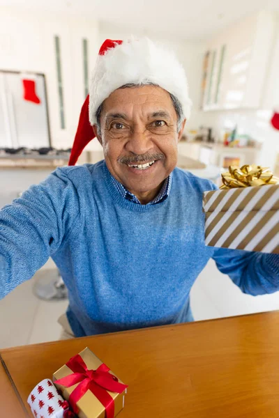 ビデオ通話中にクリスマスプレゼントを保持サンタの帽子の笑顔シニア出生男の垂直 クリスマス グローバルなコミュニケーション 包括性とシニアライフスタイルの概念 — ストック写真