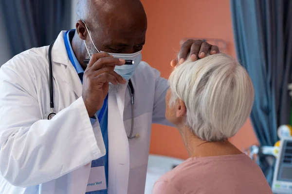 ペンライト コピースペースを持つ高齢女性患者の目を調べる多様なシニア男性医師 医療サービス — ストック写真