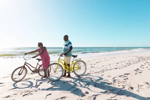 骑自行车在海滩上与晴朗的天空散步和交谈的非洲裔美国老年夫妇 复制空间 积极的生活方式 — 图库照片