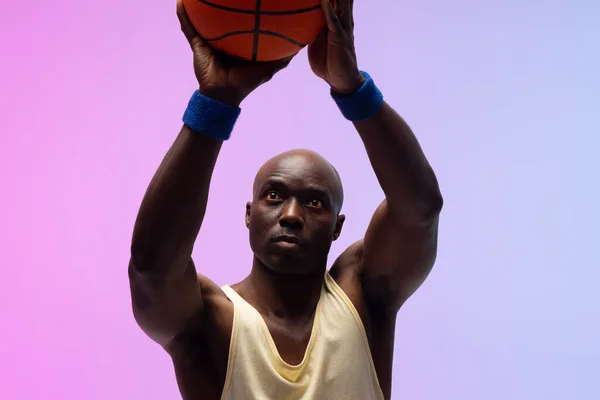 ネオンパープルからピンクの背景にバスケットボールを持つアフリカ系アメリカ人のバスケットボール選手のイメージ スポーツ 競技の概念 — ストック写真