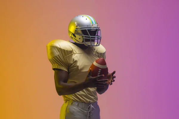 Afroamerykanin Męski Amerykański Piłkarz Trzyma Piłkę Neonowym Żółtym Fioletowym Oświetleniem — Zdjęcie stockowe