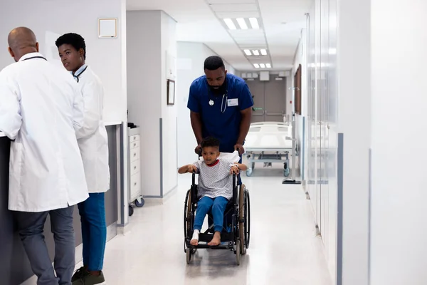 Pionowy Afrykański Amerykański Lekarz Pchający Chłopca Wózku Inwalidzkim Korytarzu Usługi — Zdjęcie stockowe