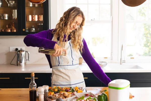 快乐的高加索女人穿着围裙站在厨房里 在切碎的蔬菜上涂上油 家庭生活 食物和健康饮食 独自呆在家里 — 图库照片