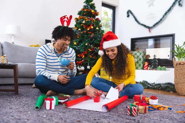 幸せなアフリカ系アメリカ人のカップルのリビングルームとパッキングプレゼントで床に座って 一緒にクリスマスに質の高い時間を過ごす — ストック写真