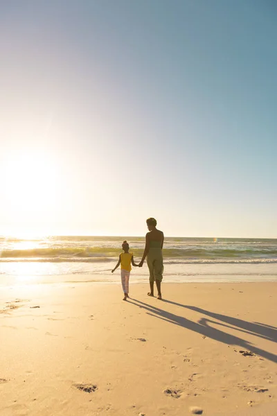 アフリカ系アメリカ人の母親と娘が手を取り合い 日没時に海に向かって歩く様子 コピースペース 変更されていない 澄んだ空 一緒に ビーチ 子供時代と自然コンセプト — ストック写真