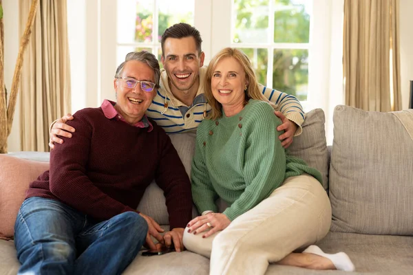 照片上是快乐的高加索父母和坐在沙发上笑着的成年儿子 家庭与共同度过美好时光的概念 — 图库照片
