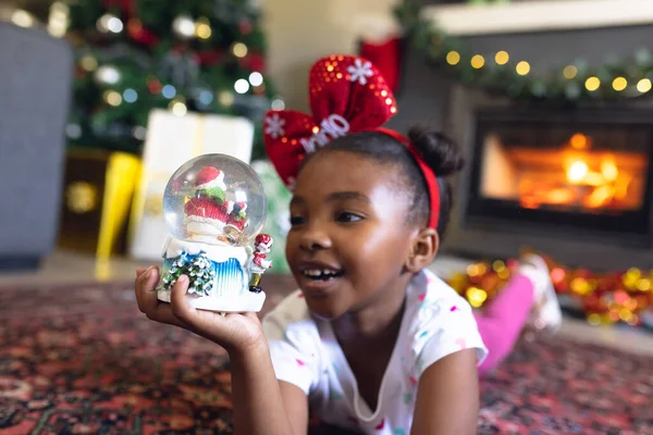 快乐的非洲裔美国女孩拿着圣诞雪球坐在旁边的壁炉边 圣诞节 童年和庆祝概念 — 图库照片