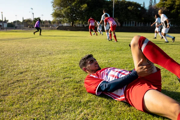 身体受伤的多种族球员躺在草地上 队友在后台打球 团队运动 竞赛和体育概念 — 图库照片