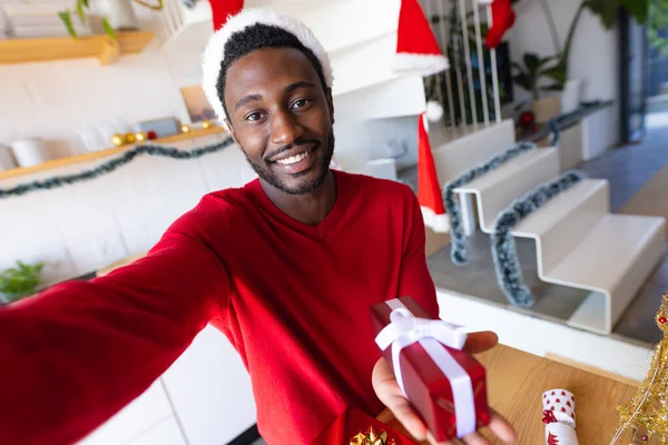 快乐的非洲裔美国人戴着圣塔克洛斯帽 拿着礼物和视频通话 圣诞时独自在家度过美好的时光 — 图库照片