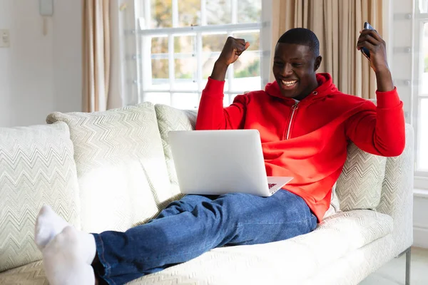 アフリカ系アメリカ人の男性が自宅のノートパソコンと応援を見てソファに横たわっていた 包括性 国内生活 自由な時間とリラクゼーション 自宅で一人で時間を過ごす — ストック写真