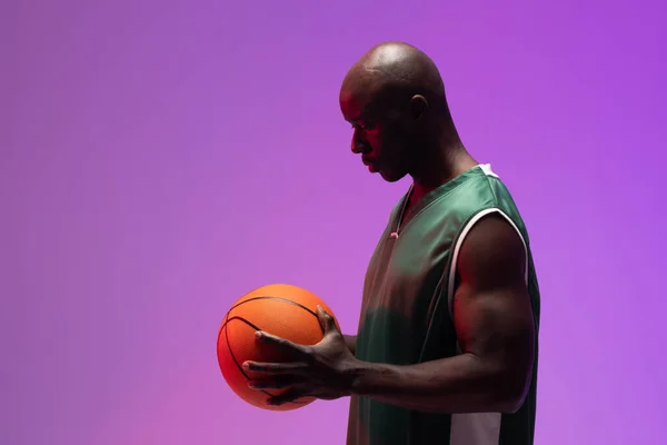 Image of african american basketball player with basketball on neon purple background. Sports and competition concept.