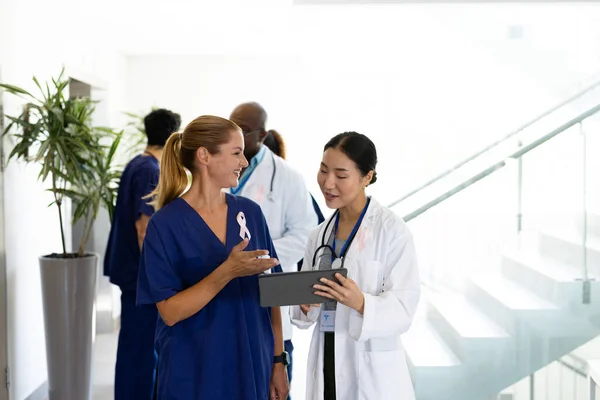 Duas Médicas Sorrindo Diversas Olhando Para Tablet Conversando Corredor Hospitalar — Fotografia de Stock