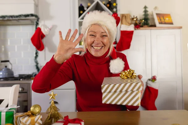 快乐的资深高加索女人戴着圣塔克洛斯帽 有视频通话 圣诞时独自在家度过美好的时光 — 图库照片