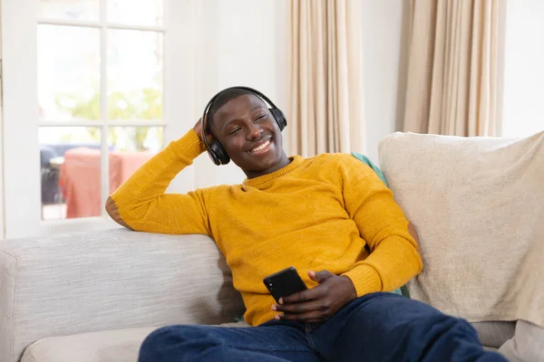헤드폰을 스마트폰을 아프리카 미국인을 미소짓고 있습니다 집에서 보내는 — 스톡 사진