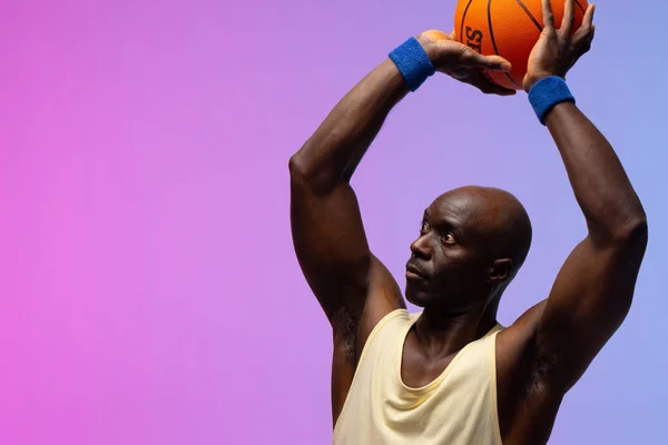 Image of african american basketball player with basketball on neon purple to pink background. Sports and competition concept.
