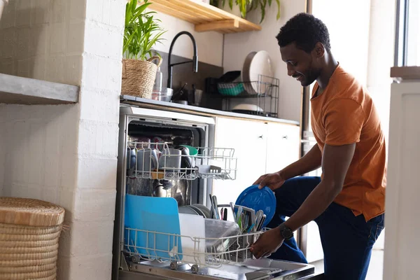 Mutlu Afro Amerikan Adam Mutfakta Durup Bulaşık Makinesini Boşaltıyor Evde — Stok fotoğraf