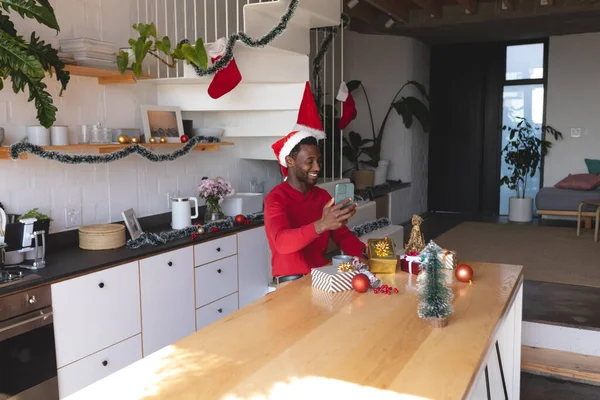 快乐的非洲裔美国人戴着圣塔帽 用智能手机打视频电话 圣诞节时一个人呆在家里 — 图库照片