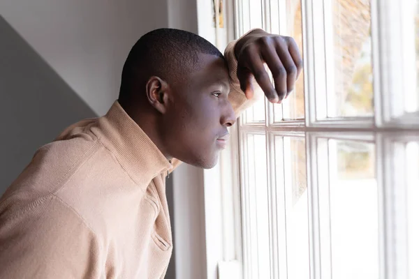 家にもたれかかって窓の外を見ているアフリカ系アメリカ人の思慮深い男 包容力国内生活孤独うつ病家で一人で過ごす時間 — ストック写真