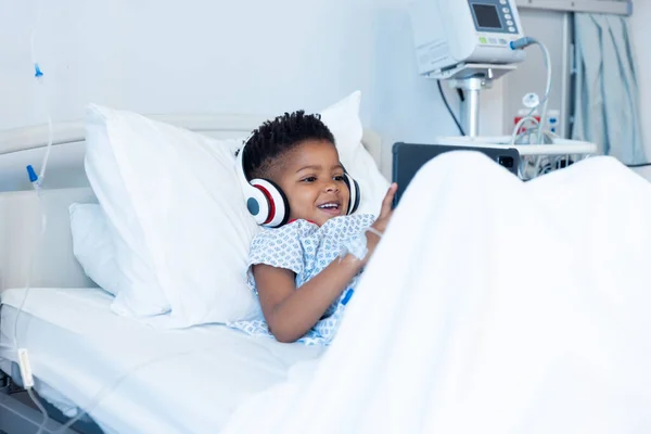 快乐的非洲男孩患者在耳机使用平板在医院的病床上与复制空间 医疗和保健服务 — 图库照片