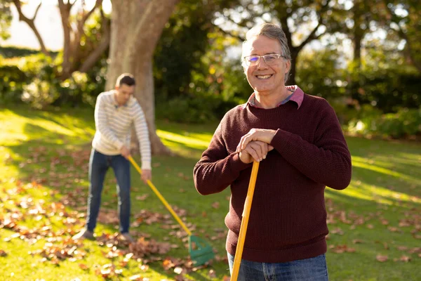 幸せな白人の父親と大人の息子が庭で葉をスワイプするイメージ 家族と一緒に質の高い時間を過ごすコンセプト — ストック写真