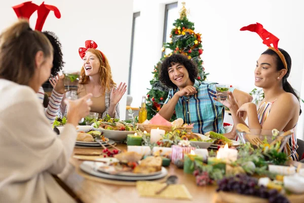 テーブルに座ってクリスマスに夕食をとる幸せな多様な友人 クリスマス お祝い 包容力とライフスタイルの概念 — ストック写真