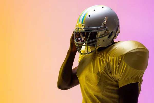 African american male american football player wearing helmet with neon yellow and purple lighting. Sport, movement, training and active lifestyle concept.