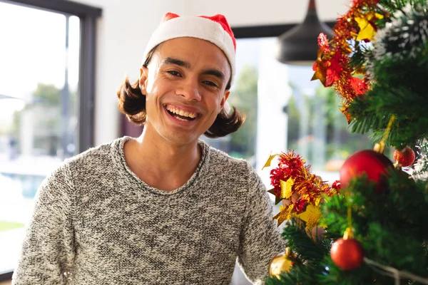 サンタの帽子をかぶった幸せな出産の男は リビングルームでクリスマスツリーを飾る クリスマスだけで質の高い時間を過ごす — ストック写真