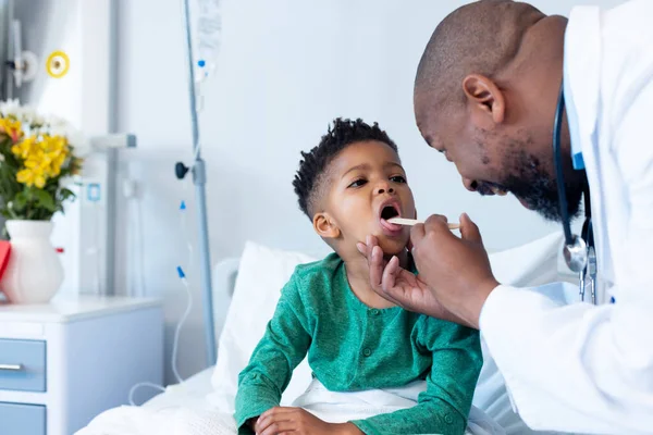 病院で少年患者の口を調べるアフリカ系アメリカ人男性医師 医療サービス — ストック写真