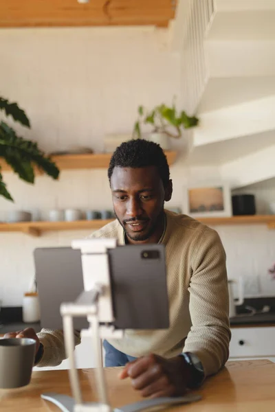 stock image Happy african american man leaning on countertop and using tablet in kitchen. Spending quality time at home alone.