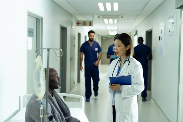 亚洲女医生和非洲老年男性患者在医院走廊里交谈 医疗和保健服务 — 图库照片
